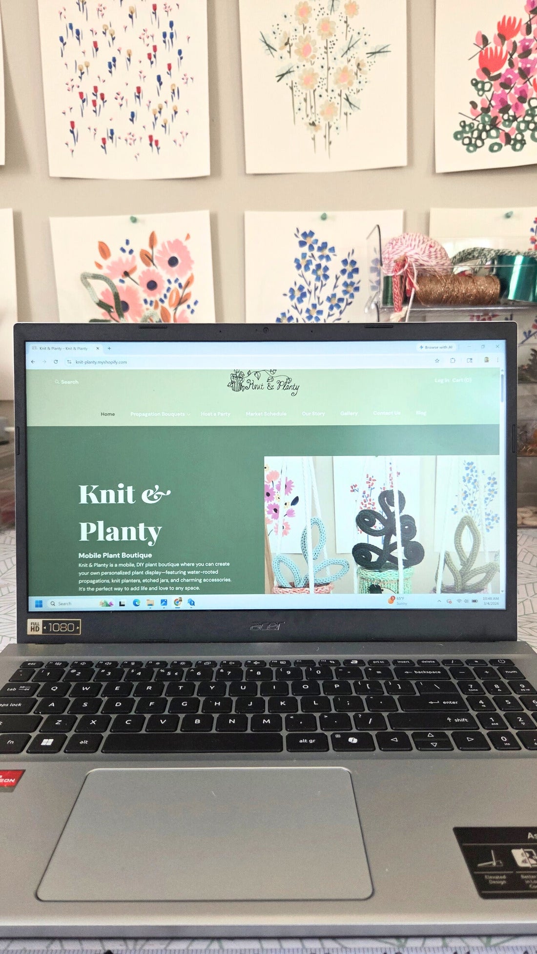 image of a laptop with the green knit & planty website shown. flower poster in the background